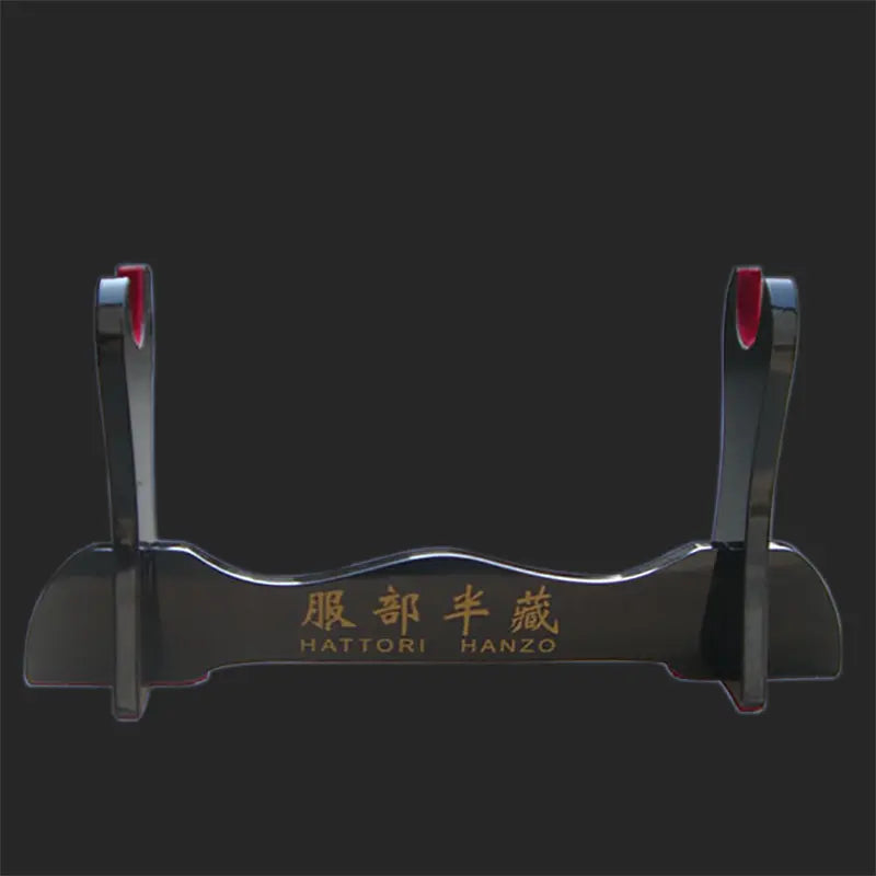 Présentoir pour katana en bois laqué noir, modèle Hattori Hanzo, photographié sur un fond noir uni, montrant le support brillant avec inscription dorée et protections rouges, utilisé comme support de sabre japonais, kake décoratif pour exposer katana, wakizashi ou shirasaya.