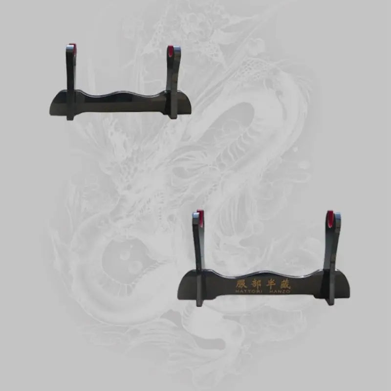 Deux présentoirs pour katana en bois noir laqué, modèle Hattori Hanzo, visibles sur un fond gris orné d’un dragon japonais en transparence, montrant les supports avec inscriptions dorées et encoches rouges, utilisés comme kake décoratifs pour exposer sabres katana, wakizashi ou shirasaya.