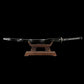 Japanese handmade katana Renge no Ken displayed on a wooden stand against a deep black background, black glossy saya with white lacquer splash patterns, katana fully sheathed, black tsuka wrapped with black cord over white ray skin, lotus motif tsuba in dark metal, traditional Japanese sword presented horizontally  
