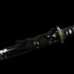 Close-up of the Japanese handmade katana Renge no Ken on a deep black background, black glossy saya with white lacquer splash patterns, katana partially sheathed, black sageo cord tied around the scabbard, dark metal lotus-pattern tsuba and gold-accented habaki visible, traditional Japanese sword fittings shown in detail
