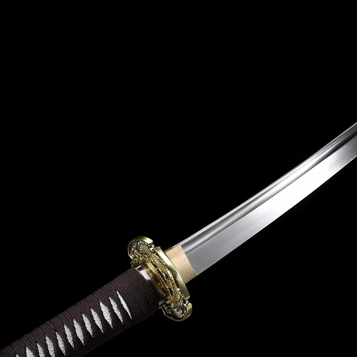 Angled close-up of the Ryusei Japanese katana focusing on the junction between the blade and the handle, photographed against a solid black background. The polished 1060 carbon steel blade extends from a gold-colored habaki with a clean, matte finish. The dragon-themed tsuba is visible in partial profile, showing engraved relief details in gold and dark metal tones. The handle is wrapped in dark brown cord over white ray skin panels, emphasizing the traditional construction and precise assembly of this Japa