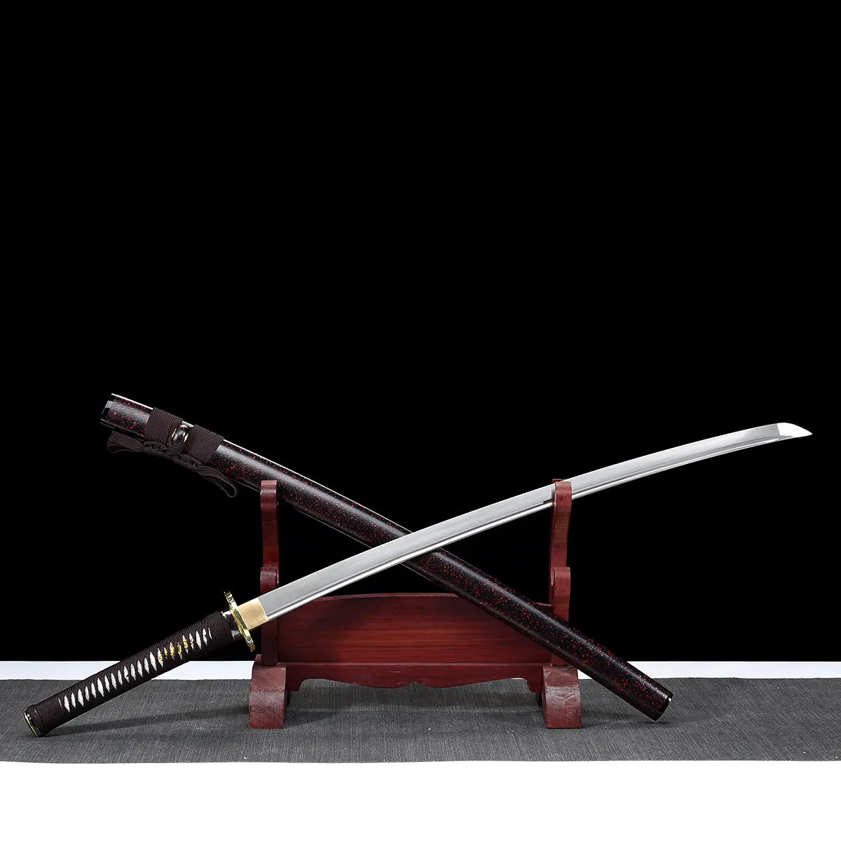 Ryusei Japanese katana displayed diagonally on a dark red wooden stand against a solid black background. The polished steel blade is fully unsheathed and crossed over its scabbard, showing a visible bohi and a curved kissaki. The saya is dark brown lacquered with black grain texture, positioned beneath the blade. The handle is wrapped in dark brown cord over white ray skin panels, fitted with a gold-colored dragon tsuba and matching habaki, highlighting the contrast between blade, fittings, and traditional 