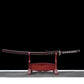 Full view of the Ryusei Japanese katana displayed horizontally on a dark red wooden stand, set against a solid black background. The sword is shown with its scabbard, featuring a dark brown lacquered saya with subtle black grain texture. The handle is wrapped in dark brown cord over white ray skin panels, with a gold-colored dragon tsuba and matching habaki. The blade is not visible, fully sheathed, highlighting the overall proportions and traditional mounting of this handcrafted Japanese katana.
