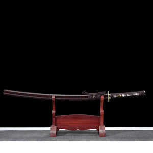 Full view of the Ryusei Japanese katana displayed horizontally on a dark red wooden stand, set against a solid black background. The sword is shown with its scabbard, featuring a dark brown lacquered saya with subtle black grain texture. The handle is wrapped in dark brown cord over white ray skin panels, with a gold-colored dragon tsuba and matching habaki. The blade is not visible, fully sheathed, highlighting the overall proportions and traditional mounting of this handcrafted Japanese katana.
