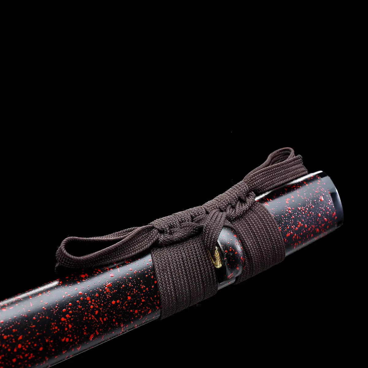 Close-up detail of the Ryusei Japanese katana scabbard photographed against a solid black background. The saya features a dark brown to black lacquered finish with red speckled grain texture. A dark brown sageo is tightly wrapped and knotted around the scabbard, showing its woven texture and traditional tying method. The kurikata is partially visible, highlighting the refined finish and understated elegance of this handcrafted Japanese katana.
