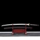 Unsheathed Ryusei Japanese katana displayed horizontally on a dark red wooden stand against a solid black background. The polished steel blade is fully visible, slightly curved, with a clean shinogi line and bohi running along the blade. The scabbard rests below the blade, showing a dark brown lacquered saya with black grain texture. The handle features dark brown cord wrapping over white ray skin panels, finished with a gold-colored dragon tsuba and matching habaki, highlighting the traditional mounting an