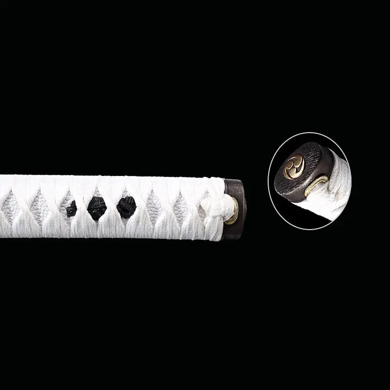 Détail de l’extrémité de la poignée du katana japonais artisanal Shinobi no Kiba, Le Croc du Shinobi, sur fond noir. Tsuka en cuir blanc avec tressage ito noir laissant apparaître les losanges, kashira sombre avec motif circulaire doré, finition propre et esthétique ninja sans tsuba.
