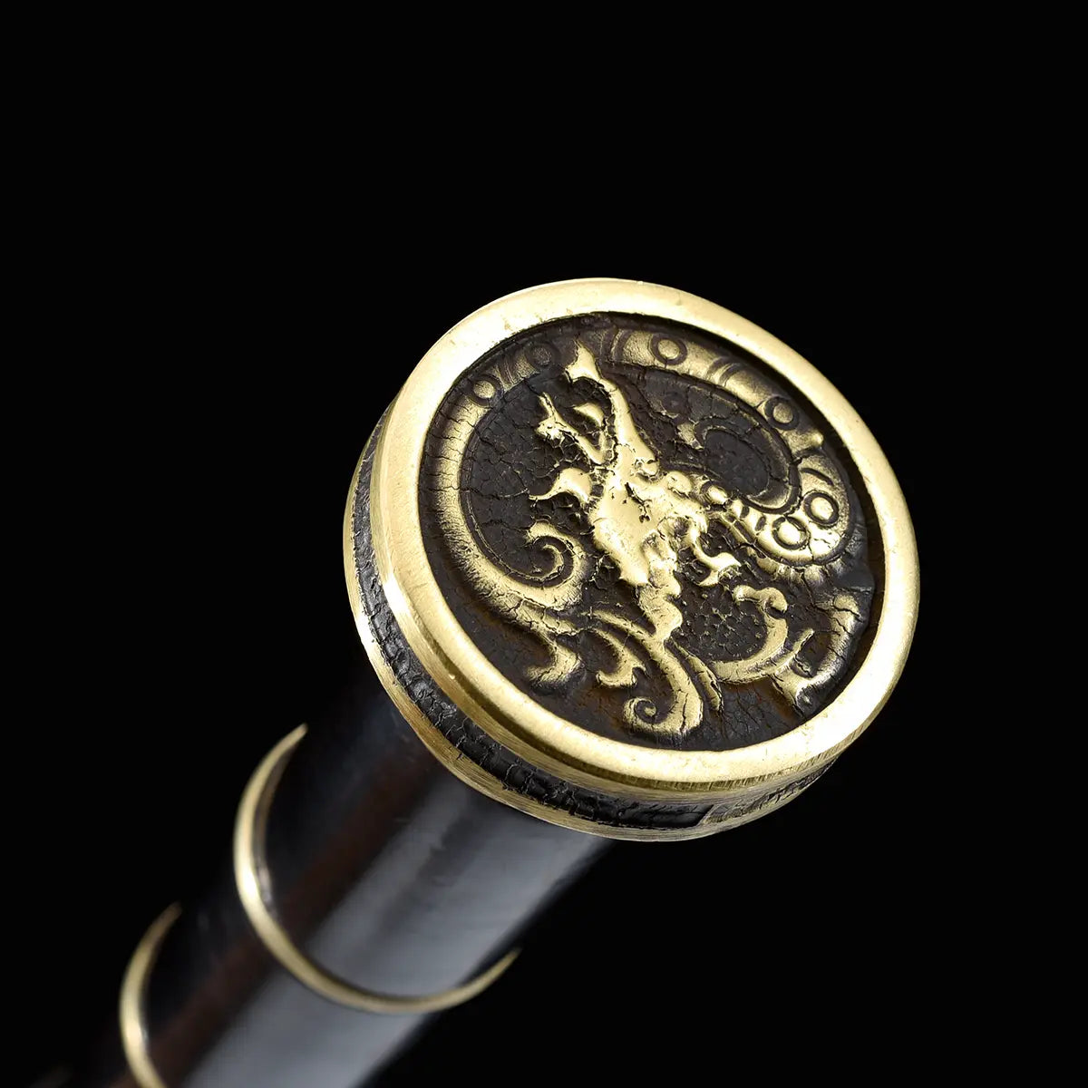 Gros plan sur le pommeau doré de l’épée chinoise Jian SHU SHENG, avec motif de dragon en relief sur fond sombre, poignée noire segmentée et anneaux en laiton, présenté sur fond noir pour montrer les détails décoratifs du Jian chinois.