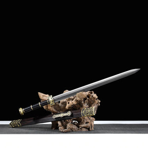 Épée chinoise Jian SHU SHENG présentée sur support en bois naturel, avec lame droite en acier plié Damas moderne, poignée noire, fourreau noir style ébène et garnitures en laiton doré, sur surface grise devant un fond noir.