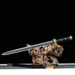 Épée chinoise Jian SHU SHENG présentée avec lame droite en acier plié Damas moderne sur support en bois naturel, fourreau noir style ébène posé en dessous, garnitures en laiton doré et fond noir avec surface grise.