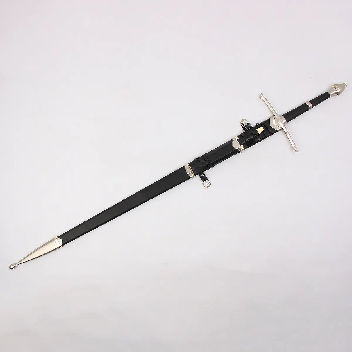 Vue complète de l’épée Strider inspirée d’Aragorn dans Le Seigneur des Anneaux, présentée en diagonale sur un fond blanc neutre. L’épée est rangée dans un fourreau noir mat avec garnitures métalliques argentées et embout poli. La poignée est gainée de cuir noir avec un pommeau métallique et une garde en croix légèrement courbée. Une petite dague est intégrée au fourreau avec des sangles en cuir visibles.

