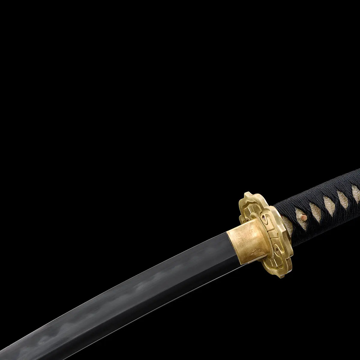 Close-up detail of the Japanese tachi katana Taiyo Taisho photographed on a deep black background, showing the polished steel blade with a visible natural hamon line, gold-colored brass habaki fitted against the blade, ornate gold tsuba with carved details, and black tsuka wrapped in black ito over white ray skin panels, studio lighting highlighting the steel texture and traditional fittings
