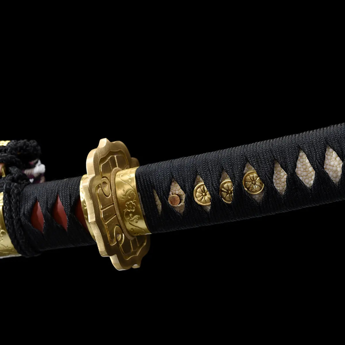 Close-up detail of the Japanese tachi katana Taiyo Taisho photographed on a deep black background, focusing on the handle wrapped in black ito over white ray skin panels, with gold-colored menuki aligned along the tsuka, ornate gold fuchi and tsuba partially visible, and subtle texture of the wrapping clearly defined, studio lighting highlighting the materials, craftsmanship, and traditional Japanese handle construction
