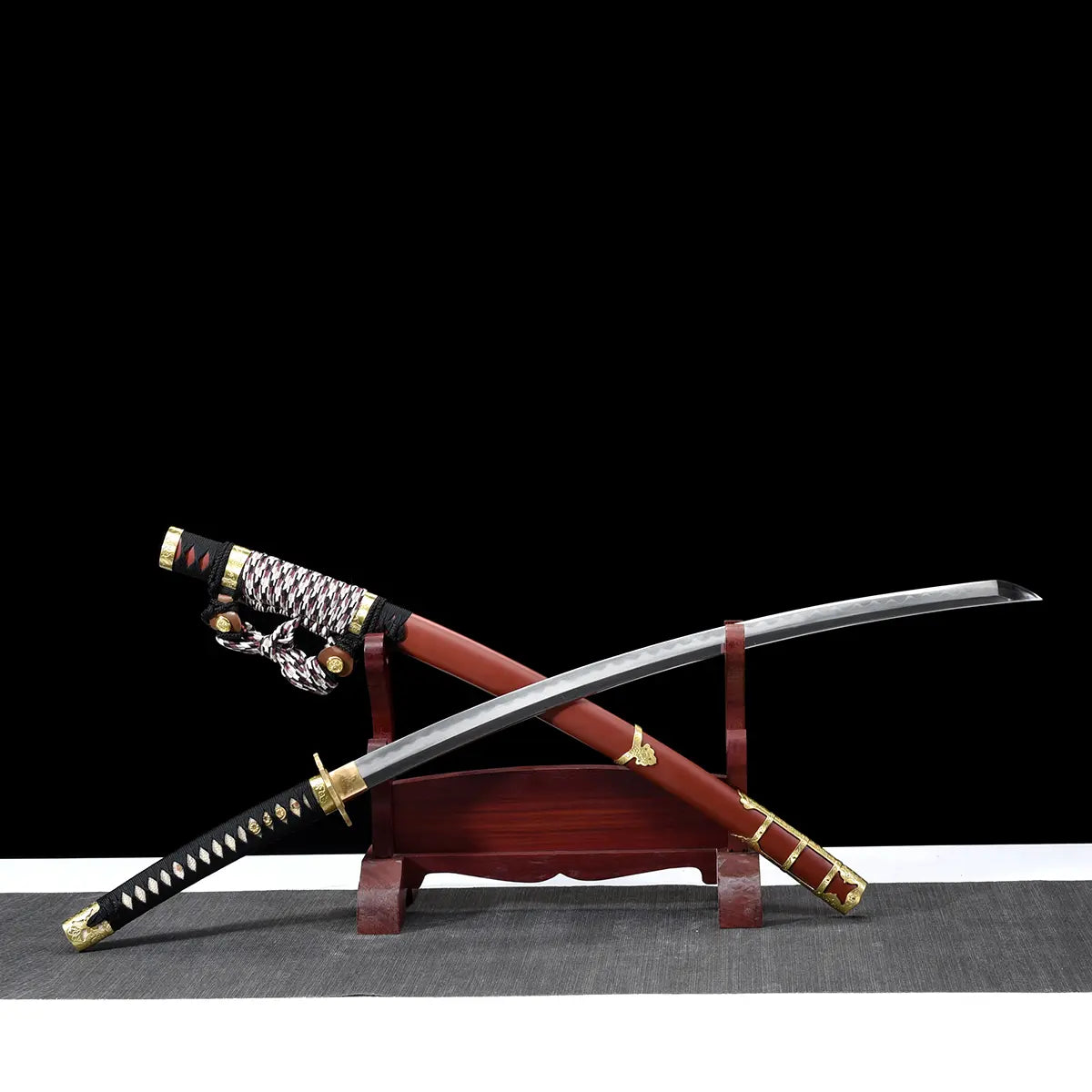 Japanese tachi katana Taiyo Taisho displayed crossed on a traditional red wooden sword stand, with the unsheathed curved steel blade featuring a visible hamon crossing over the red lacquered saya with gold fittings, braided sageo cord resting near the handle, black tsuka with white ray skin panels and gold menuki, photographed in studio on a deep black background
