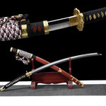 Japanese tachi katana Taiyo Taisho presented in a crossed composition on a traditional red wooden sword stand, showing the unsheathed curved steel blade with visible hamon crossing over the red lacquered saya with gold fittings, braided black white and red sageo cord resting near the handle, black tsuka with white ray skin panels and gold menuki, photographed in studio on a deep black background with a gray surface, highlighting curvature, balance, and traditional Japanese craftsmanship
