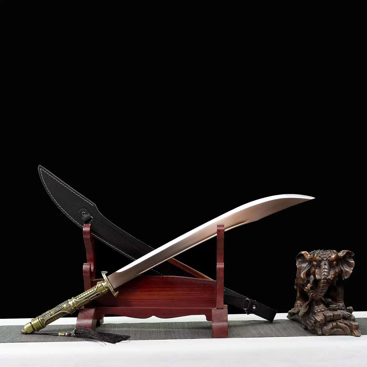 Sabre chinois Dao TIAN DAO avec lame courbe sortie du fourreau, posé en diagonale sur un support en bois rouge, poignée dorée rétro-futuriste, garde métallique, fourreau noir à coutures blanches en arrière-plan et figurine d’éléphant décorative sur fond noir.