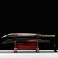 Sabre chinois Dao TIAN DAO présenté lame sortie au-dessus du fourreau noir courbe, avec poignée dorée rétro-futuriste, garde métallique, pompon noir suspendu, support en bois rouge et fond noir.