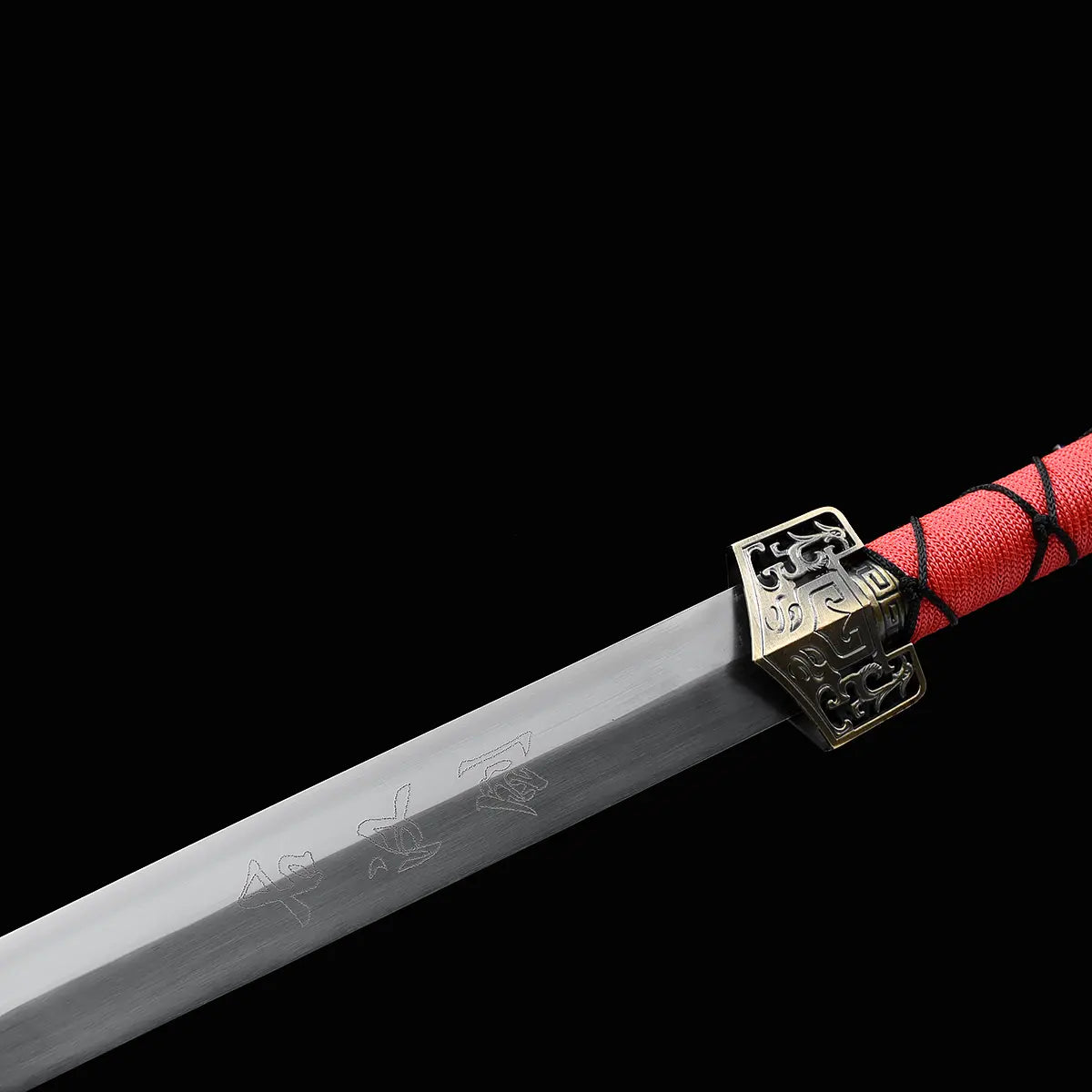 Gros plan sur l’épée chinoise Jian TIAN LONG avec lame droite en acier gravée de l’inscription chinoise « 龙泉剑 » signifiant Longquan Jian, garde métallique décorée et poignée rouge entourée d’un cordage noir sur fond noir.