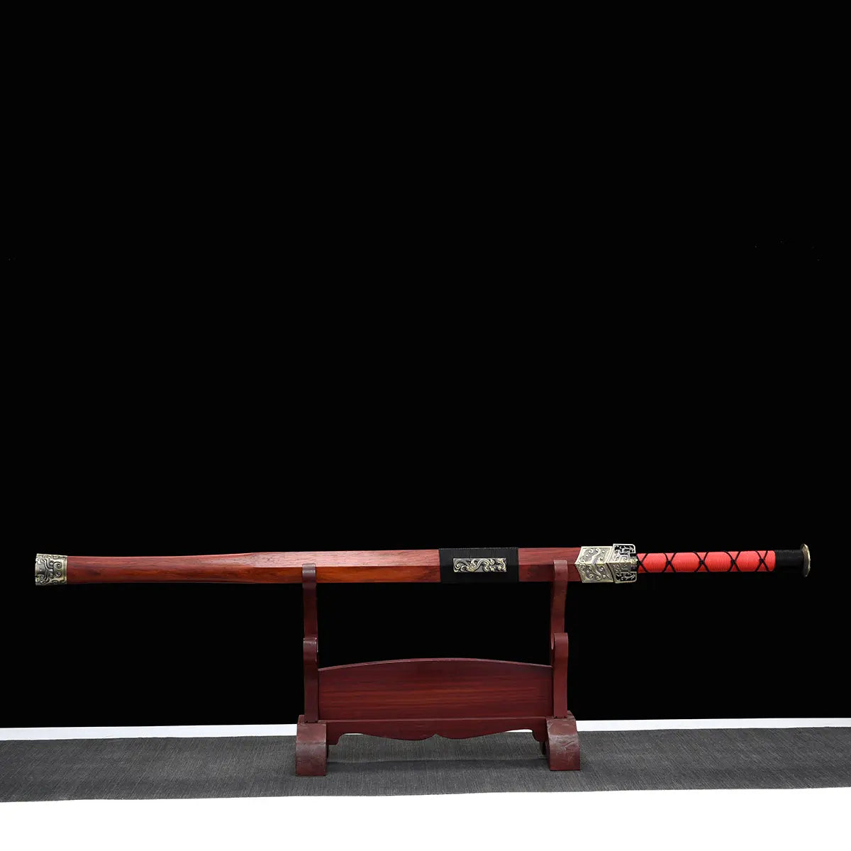 Épée chinoise Jian TIAN LONG présentée dans son fourreau en bois de rose sur un support d’exposition, avec poignée rouge entourée d’un cordage noir, garnitures métalliques décorées, fond noir et tapis gris visible en bas de l’image.