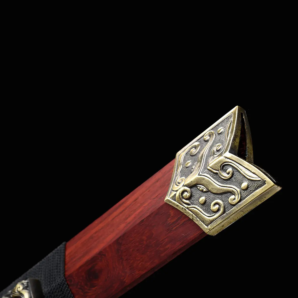 Gros plan sur l’extrémité du fourreau en bois de rose de l’épée chinoise Jian TIAN LONG, avec garniture métallique décorée de motifs gravés, finition bronze vieilli et texture rouge-brun du bois sur fond noir.