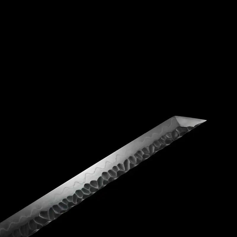 Gros plan de la pointe (kissaki) du wakizashi Hoshizora : lame acier T10 trempe à l’argile avec hamon ondulé bien visible et texture martelée tsuchime ; angle de pointe type tanto, éclairage latéral ; fond noir minimaliste — sabre japonais artisanal Blade Bushido.