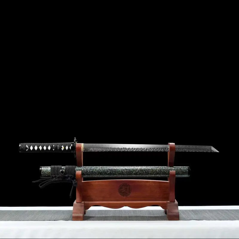 Wakizashi japonais Hoshizora présenté lame dégainée sur support en bois : hamon réel et texture tsuchime bien visibles jusqu’au kissaki, tsuka noire losanges de samegawa blanc, tsuba ronde noire ; saya laqué vert nuit effet nashiji posé en dessous. Mise en scène sur tapis gris avec bordure blanche, fond noir — sabre artisanal acier T10 trempe à l’argile, Blade Bushido.