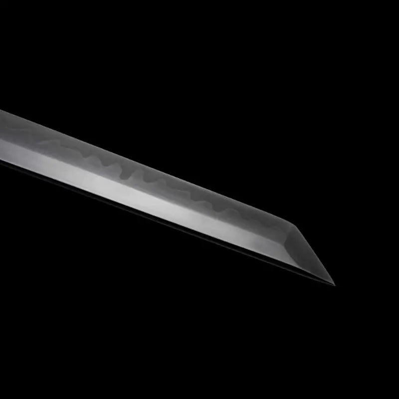 Gros plan du kissaki (pointe) du wakizashi japonais artisanal Aonami : lame T10 sans bohi, hamon bien visible jusqu’au yokote, poli miroir, photographié sur fond noir — trempe à l’argile, finition précise pour coupe nette.