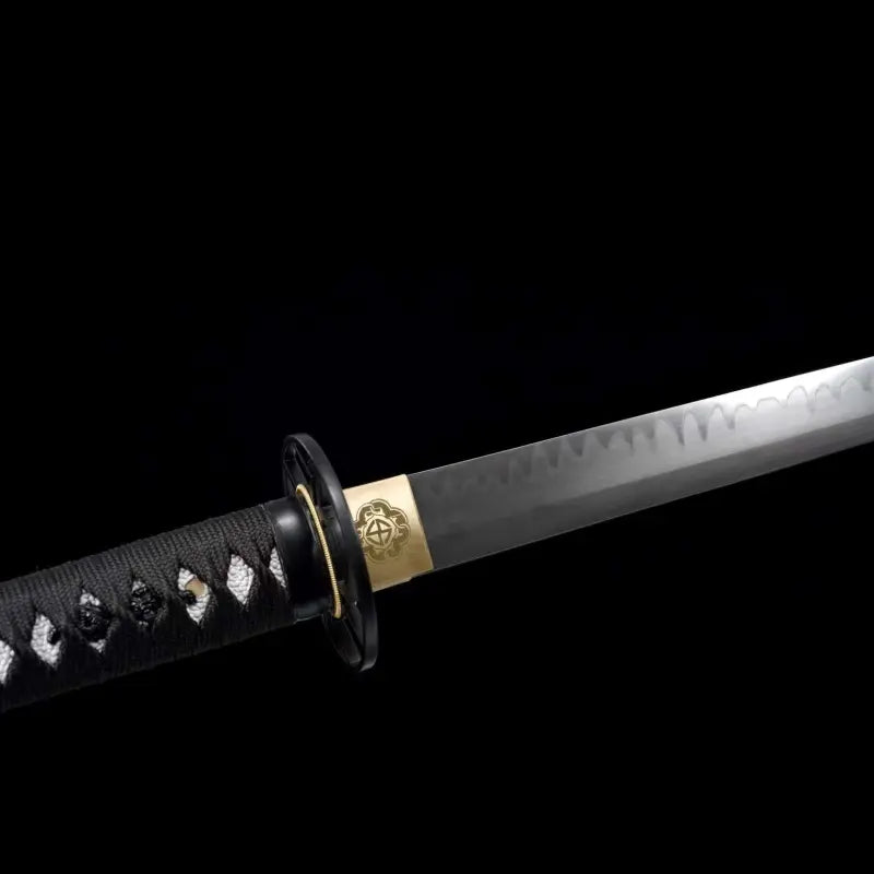 Gros plan du wakizashi japonais artisanal Aonami : tsuka en ito noir à losanges de same blanche, tsuba ronde noire, habaki en laiton gravé et lame T10 sans bohi montrant un hamon ondé ; prise de vue latérale sur fond noir.