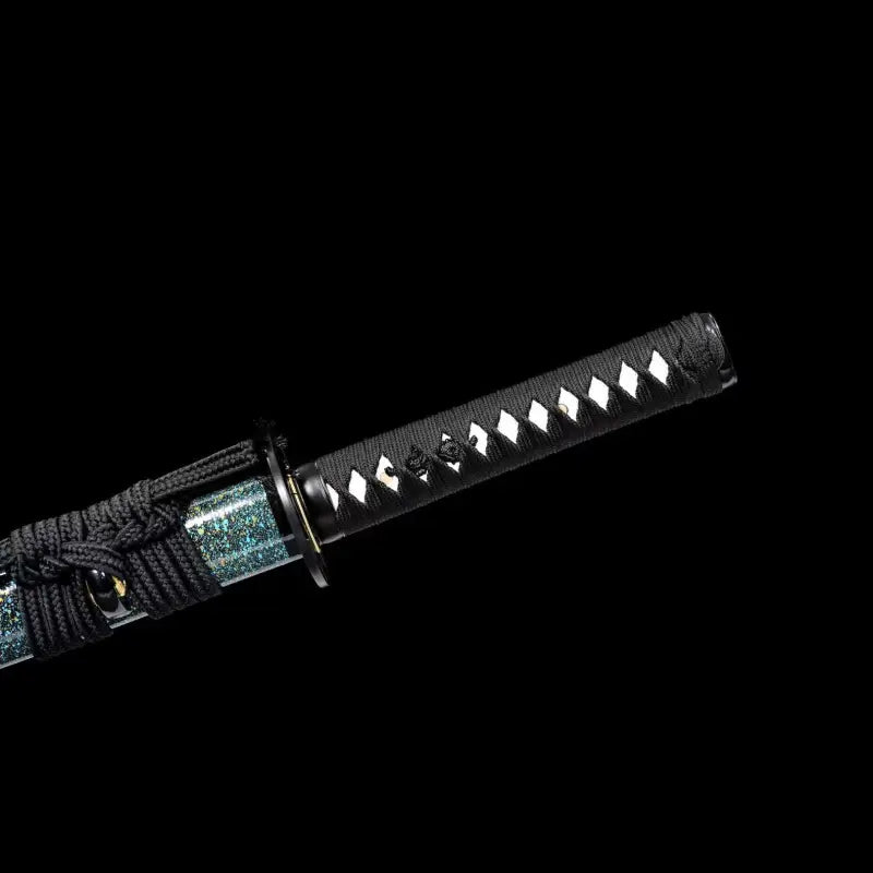 Gros plan du wakizashi japonais artisanal Aonami en acier T10 (hamon réel) : tsuka noire en ito, losanges de same blanche, tsuba ronde noire et habaki laiton, sageo noir sur saya nashiji bleu-vert, photographié sur fond noir.