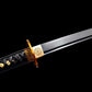 Gros plan du wakizashi japonais “Kurochiku” : habaki en laiton gravé, tsuba dorée motif bambou, tsuka à tressage noir avec menuki dorés, lame noire satinée avec bohi, sur fond noir minimaliste.