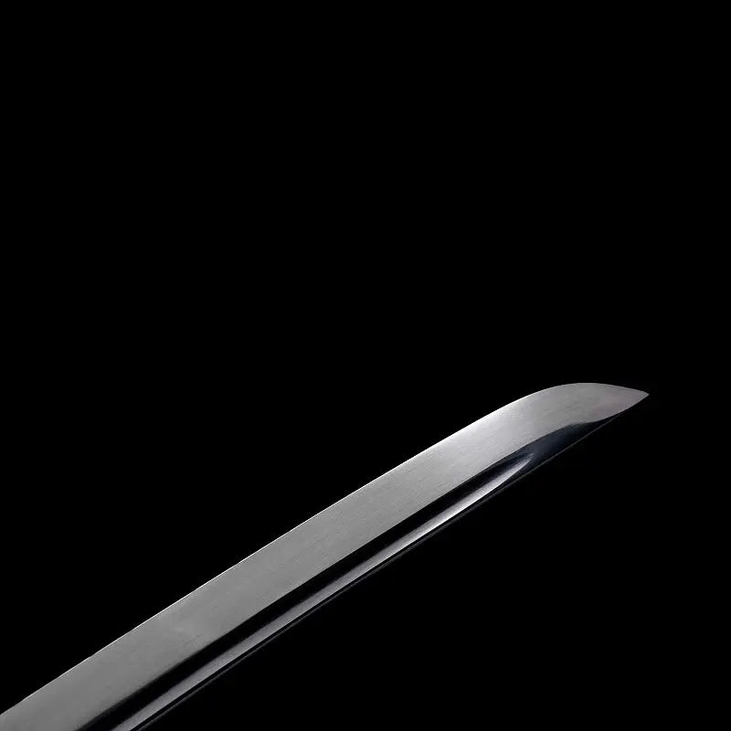 Gros plan de la pointe (kissaki) du wakizashi japonais “Kurochiku” : lame noire satinée avec bohi visible, tranchant poli, sur fond noir minimaliste.