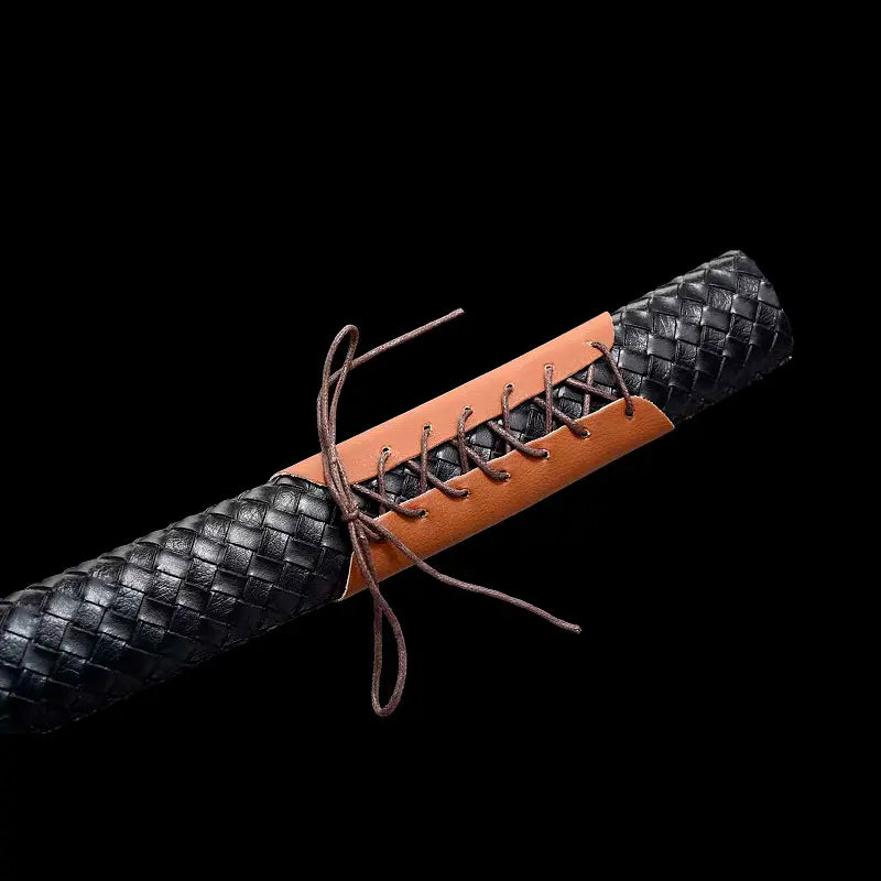 Gros plan du saya du wakizashi japonais “Kurochiku” : tressage noir façon cuir avec panneau à laçage marron au centre, texture quadrillée bien visible, sur fond noir profond pour un rendu premium.