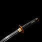 Gros plan du wakizashi japonais “Kurochiku” : tsuka tressée noire avec menuki dorés, habaki en laiton gravé, tsuba dorée motif bambou et lame noire satinée avec bohi, sur fond noir minimaliste et premium.