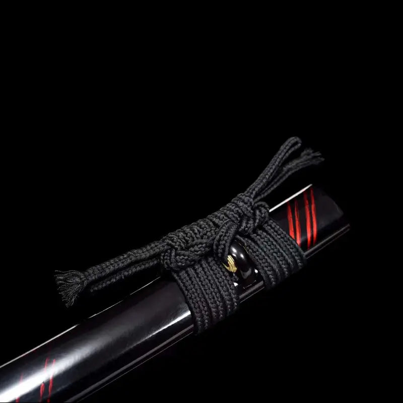 Gros plan de la saya noire laquée du wakizashi japonais Renge no Reicha, liserés pourpres brillants, nœud de sageo noir serré autour du kurikata avec shitodome en laiton, éclairage studio sur fond noir — sabre court artisanal en acier plié damassé, Blade Bushido.