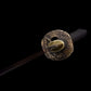 Gros plan de la tsuba en laiton motif lotus du wakizashi japonais Renge no Reicha, tsuka tressé noir, début de lame sombre en perspective, éclairage doux sur fond noir studio — sabre court artisanal acier plié damassé, Blade Bushido.