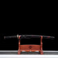 Wakizashi japonais Renge no Reicha en présentation complète : saya noire laquée à liserés pourpres, tsuka tressé noir, fittings laiton, posé sur un support en bois verni, fond noir et base gris clair — sabre court artisanal acier plié damassé, Blade Bushido.