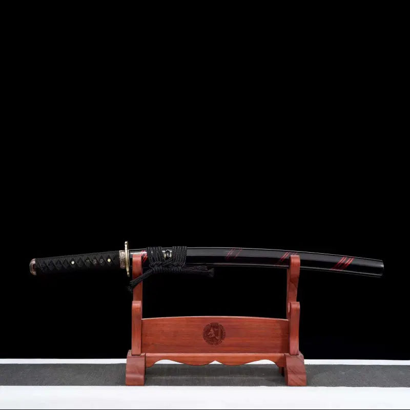 Wakizashi japonais Renge no Reicha en présentation complète : saya noire laquée à liserés pourpres, tsuka tressé noir, fittings laiton, posé sur un support en bois verni, fond noir et base gris clair — sabre court artisanal acier plié damassé, Blade Bushido.