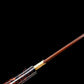 Gros plan sur l’habaki en laiton du wakizashi shirasaya « Kuro Yōgan », lame acier plié au motif damas rouge-noir en cours d’extraction du saya laqué noir-vermillon (style urushi), cadrage diagonal sur fond noir en studio.