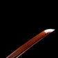 Gros plan du kissaki (pointe) d’un wakizashi shirasaya artisanal Kuro Yōgan, lame acier plié motif damas rouge-noir avec bohi courant le long du tranchant, polissage miroir bien visible, sur fond noir en studio.