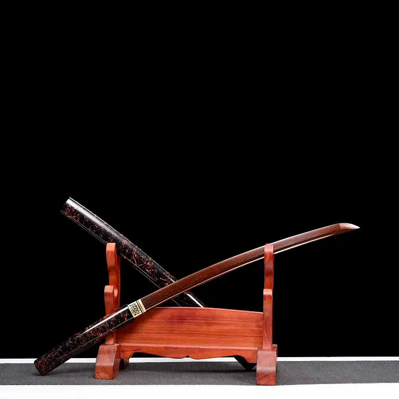Wakizashi shirasaya artisanal « Kuro Yōgan » présenté en diagonale sur un katanakake en bois, lame acier plié au motif damas rouge-noir partiellement dégainée, saya laqué urushi noir-vermillon en arrière-plan, fond noir studio, habaki en laiton visible.