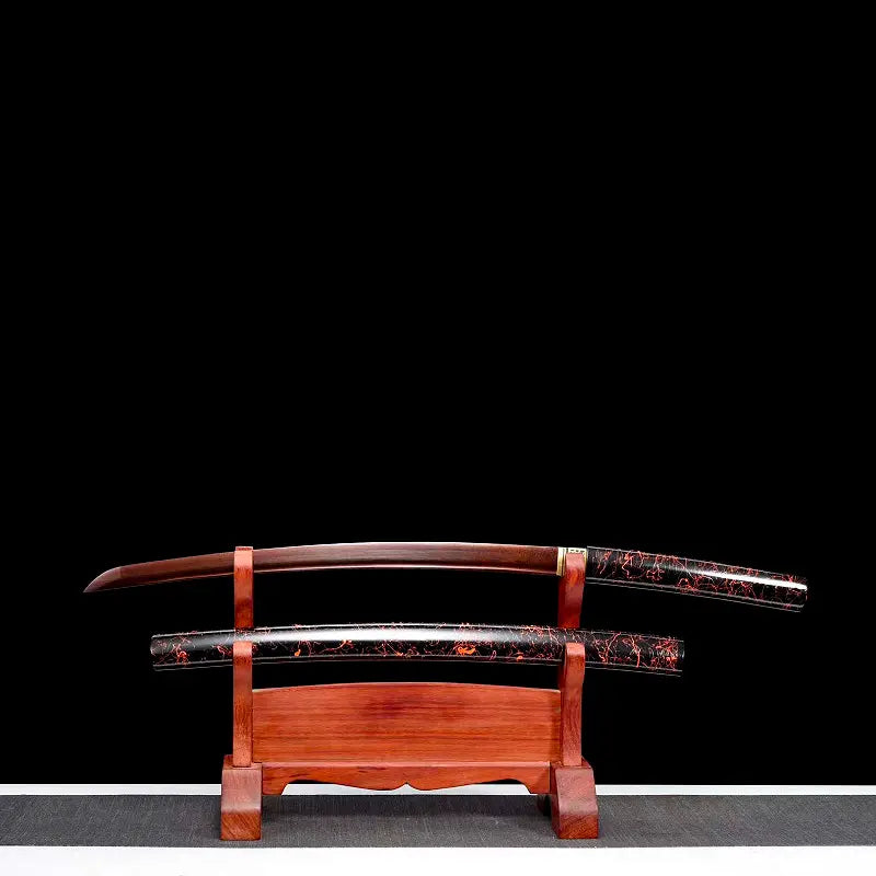 Wakizashi shirasaya artisanal « Kuro Yōgan » posé sur un katanakake en bois, lame acier plié au motif damas rouge-noir partiellement dégainée (bohi visible), saya laqué urushi noir-vermillon en dessous ; fond noir, vue frontale en studio.