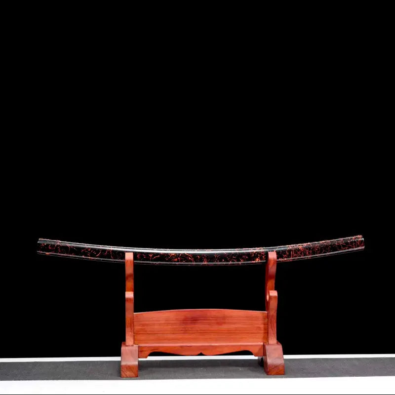 Vue d’ensemble du saya du wakizashi shirasaya artisanal Kuro Yōgan, posé seul sur un katanakake en bois teinte rouge, finition laque urushi noir-vermillon effet “lave”, fond noir avec liseré de sol gris/blanc en bas ; cadrage frontal, ambiance studio premium.