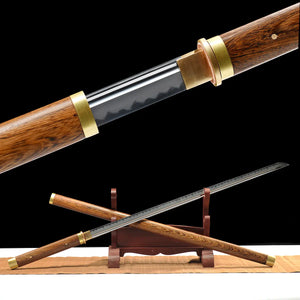 Wooden sword cane photographed on a deep black background, shown partially unsheathed to reveal a polished steel blade with a visible straight fuller and subtle hamon-like pattern. The dark brown wooden scabbard and handle display a pronounced natural wood grain, finished with gold-toned brass rings at both ends. The sword cane is positioned diagonally on a carved dark wooden display stand, resting on a light brown fabric surface, with the blade extended forward and the scabbard crossing beneath it.
