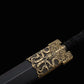 Gros plan sur les garnitures dorées de l’épée chinoise Jian XUAN LONG, avec garde décorée, entrée de fourreau noir, poignée tressée noire et motifs traditionnels en métal.