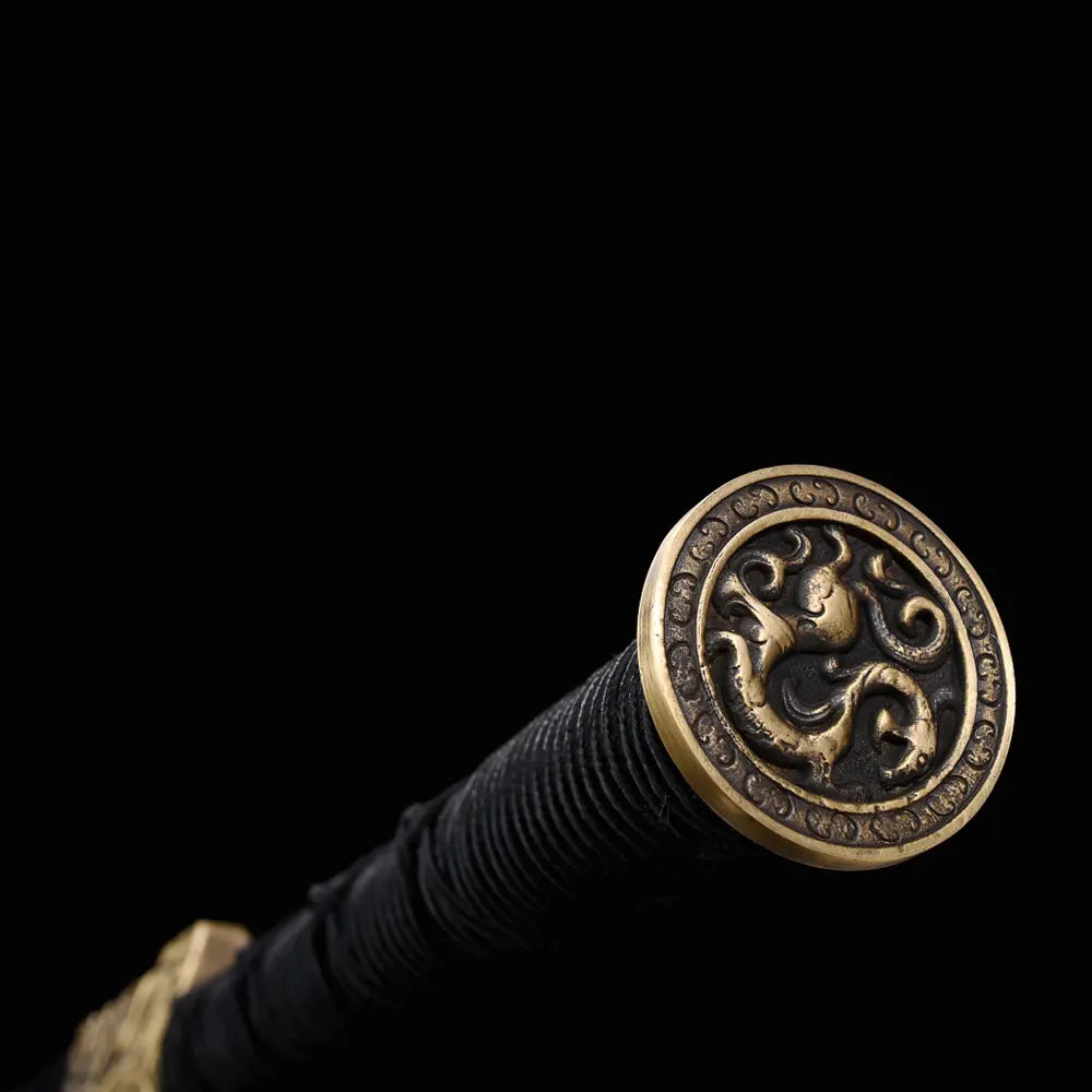 Gros plan sur le pommeau rond doré de l’épée chinoise Jian XUAN LONG, avec poignée noire tressée, motifs décoratifs en relief et fond noir sobre.