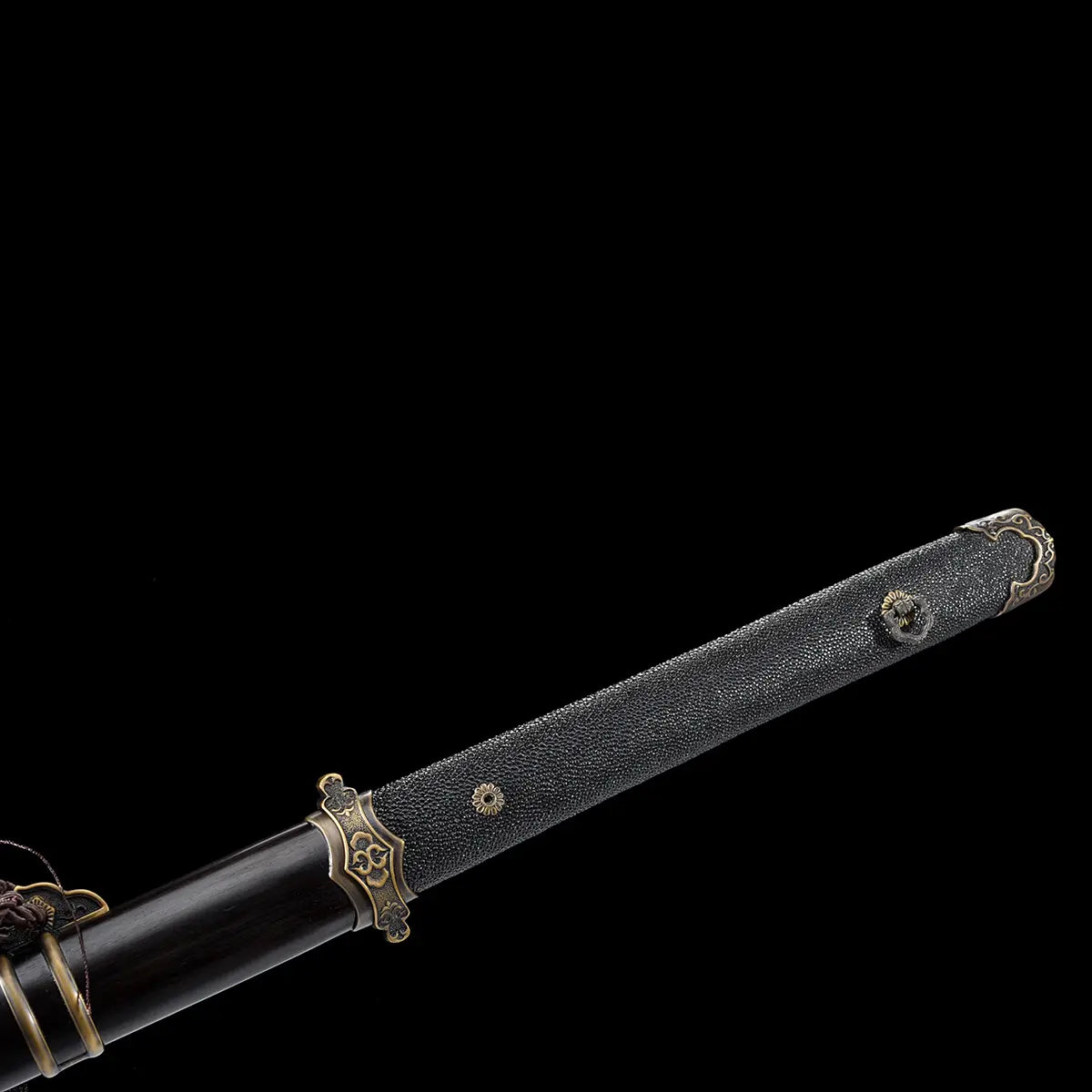 Gros plan sur la poignée noire texturée en galuchat d’une épée chinoise Jian YI XIN, avec garde en laiton vieilli, pommeau décoratif et partie du fourreau noir laqué visible. La prise de vue sur fond noir met en valeur les finitions traditionnelles, la texture de la poignée et les ornements métalliques de ce Jian chinois artisanal de collection, Tai Chi et Wushu.