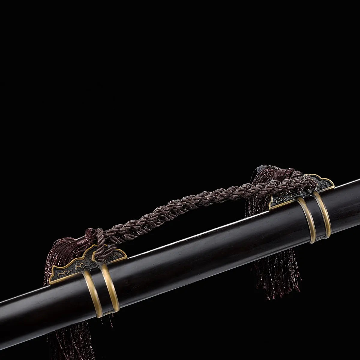 Gros plan sur le fourreau noir laqué d’une épée chinoise Jian YI XIN, avec dragonne tressée sombre, pompons décoratifs et garnitures métalliques en laiton vieilli. La prise de vue sur fond noir met en valeur les détails du fourreau et les finitions traditionnelles de ce Jian chinois artisanal de collection, Tai Chi et Wushu.