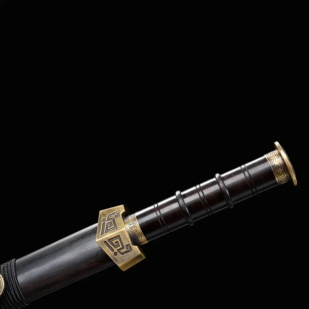 Gros plan sur la poignée noire et la garde bronze ancien de l’épée chinoise Jian ZHEN ZHAI, avec motifs géométriques gravés, fourreau noir en ébène et finition sombre sur fond noir.