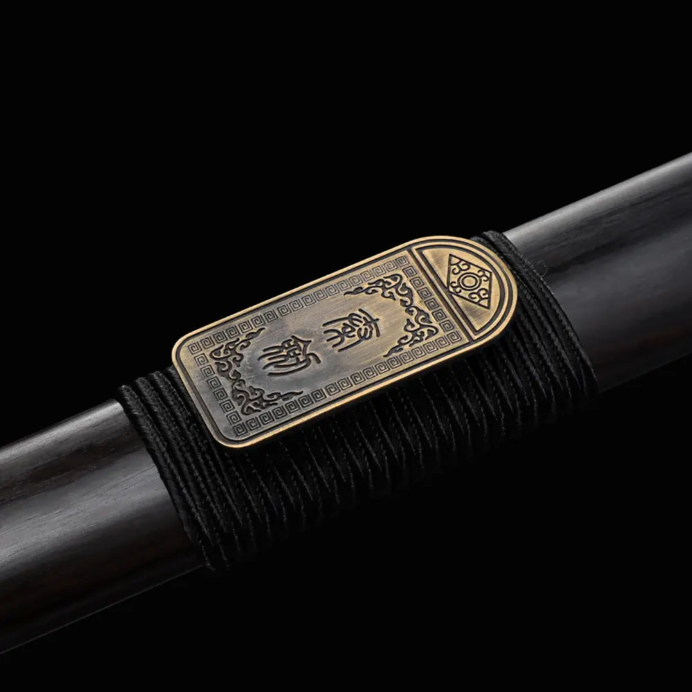 Gros plan sur la plaque gravée Zhen Zhai du fourreau noir en ébène de l’épée chinoise Jian ZHEN ZHAI, avec inscription chinoise protectrice, cordage noir et finition bronze ancien sur fond noir.
